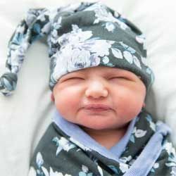 Sleeping baby wrapped in a gray floral blanket with matching hat, eyes closed and cheeks puffed.