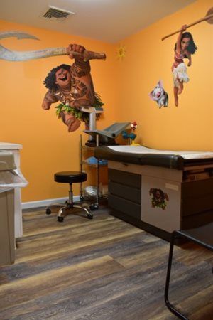 Medical exam room with orange walls, wall murals, exam table, stool, and striped flooring