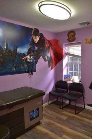 Massage room with a wall mural, treatment table, chairs, and a window under bright ceiling light