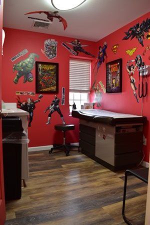 Red bedroom with superhero wall decals, a desk by the window, and wood floor
