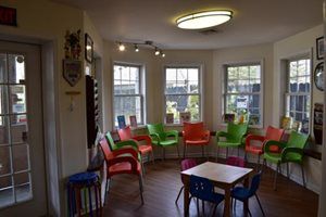 Small meeting room with colorful chairs around tables and large windows in daylight
