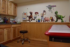 Children’s playroom with wooden cabinets, toy figures on a shelf, and a red-and-white changing table.
