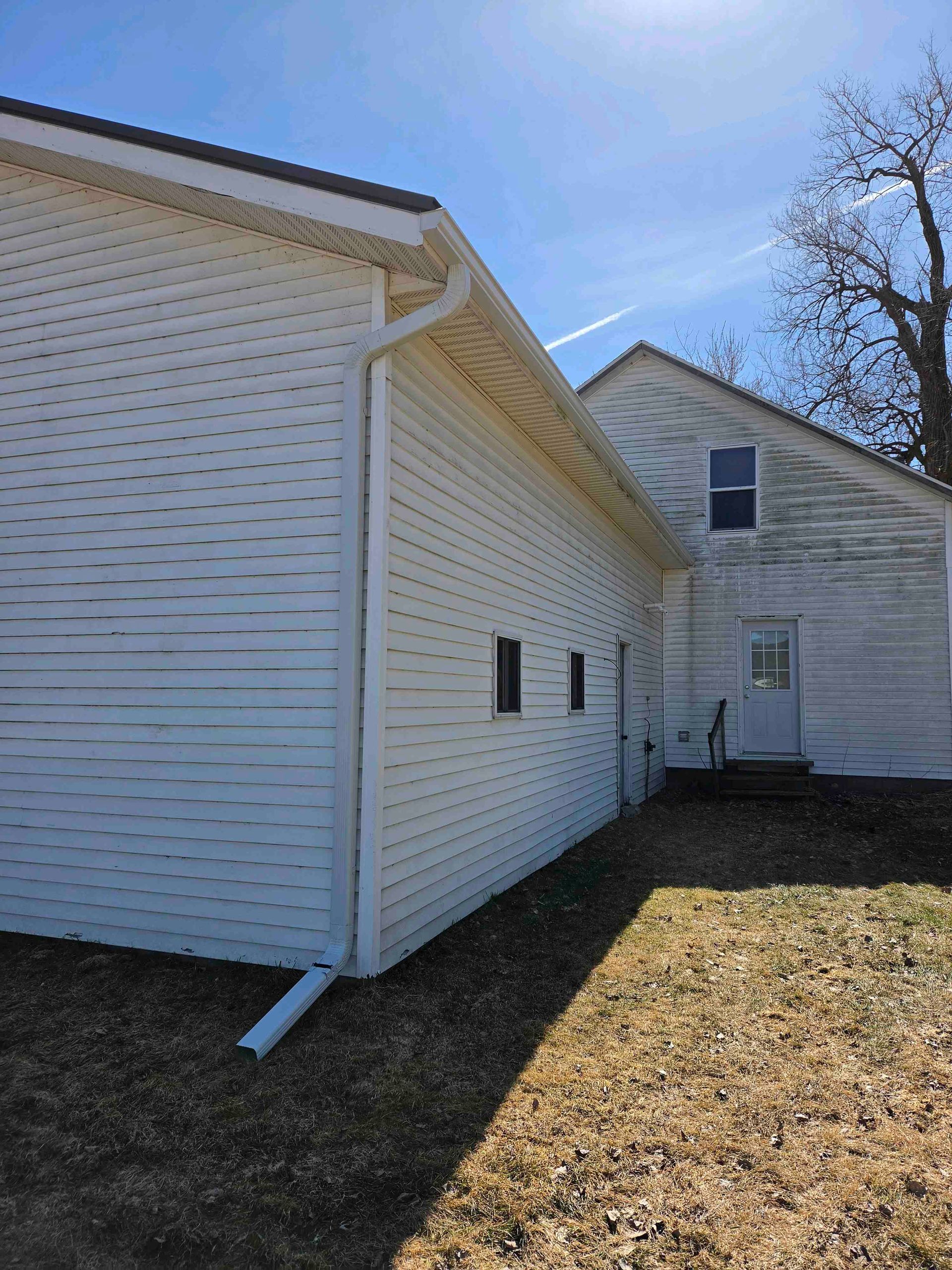 White house exterior with siding, side windows, and a sunlit yard under a blue sky