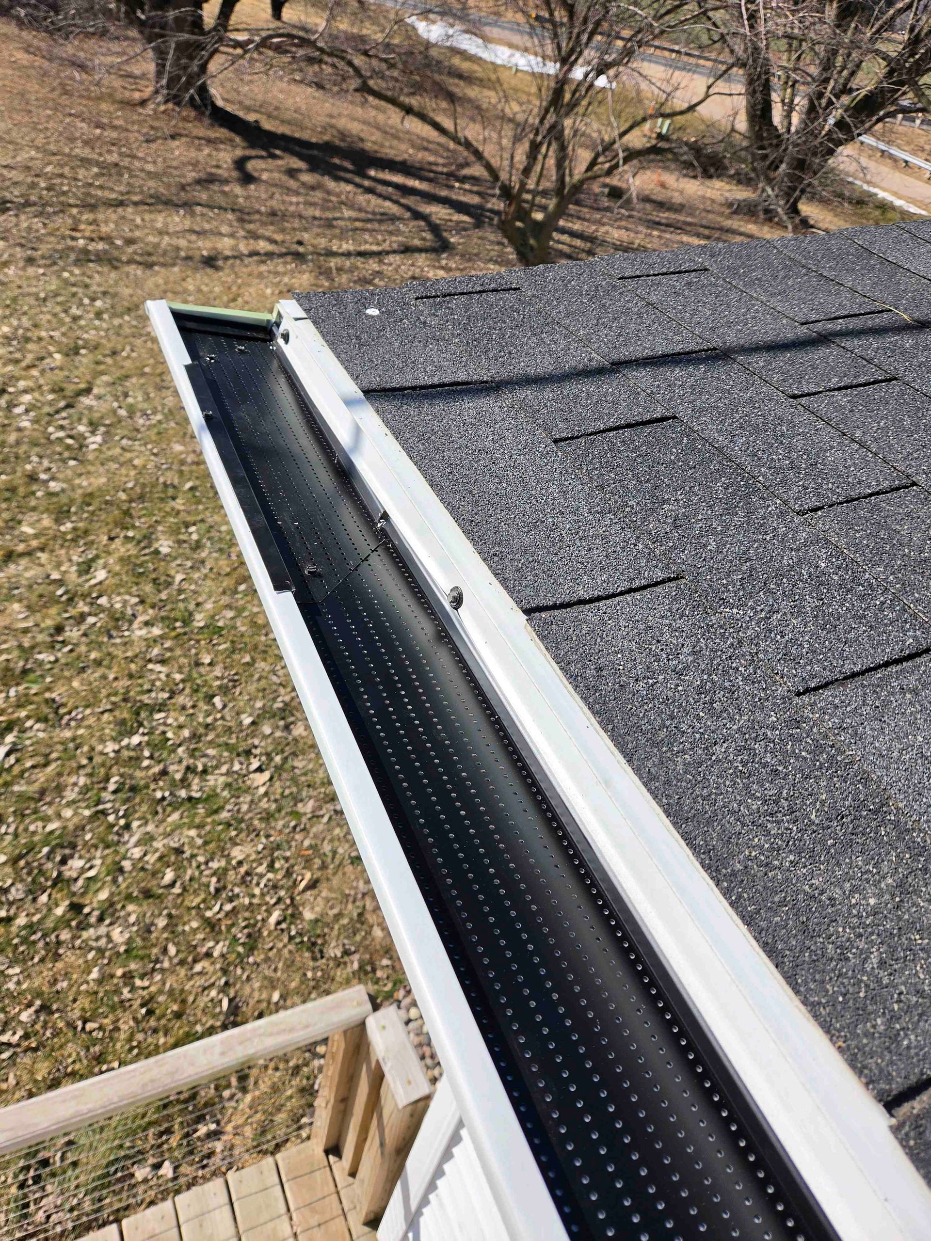 Roof gutter along a shingled roof edge beside a yard, viewed from above