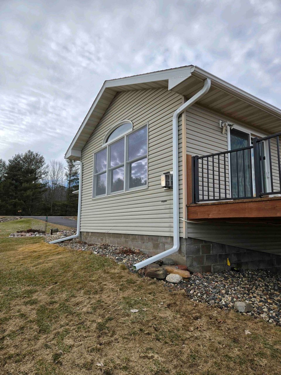 House exterior with beige siding, large windows, and a small porch under an overcast sky.