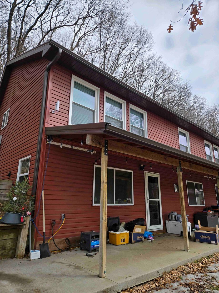 Red two-story house with a covered front porch, windows, and autumn trees overhead