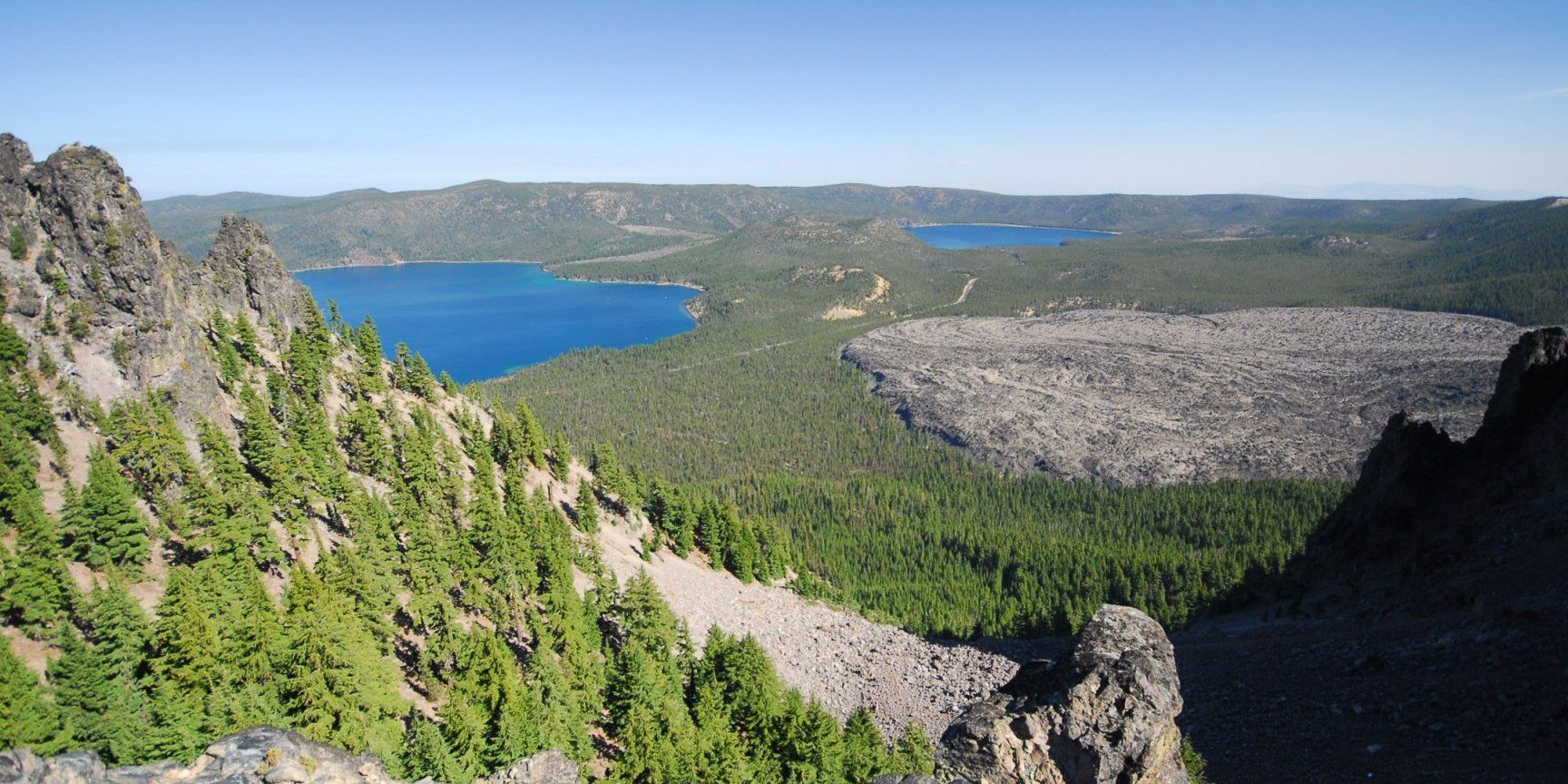 A view of a lake from the top of a mountain surrounded by trees.