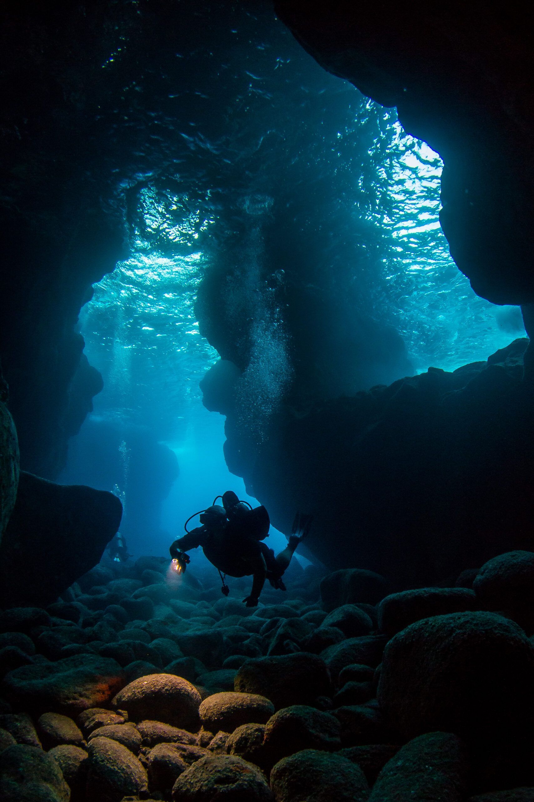 Silhouette of a scuba diver in a blue underwater cave lit by shafts of light
