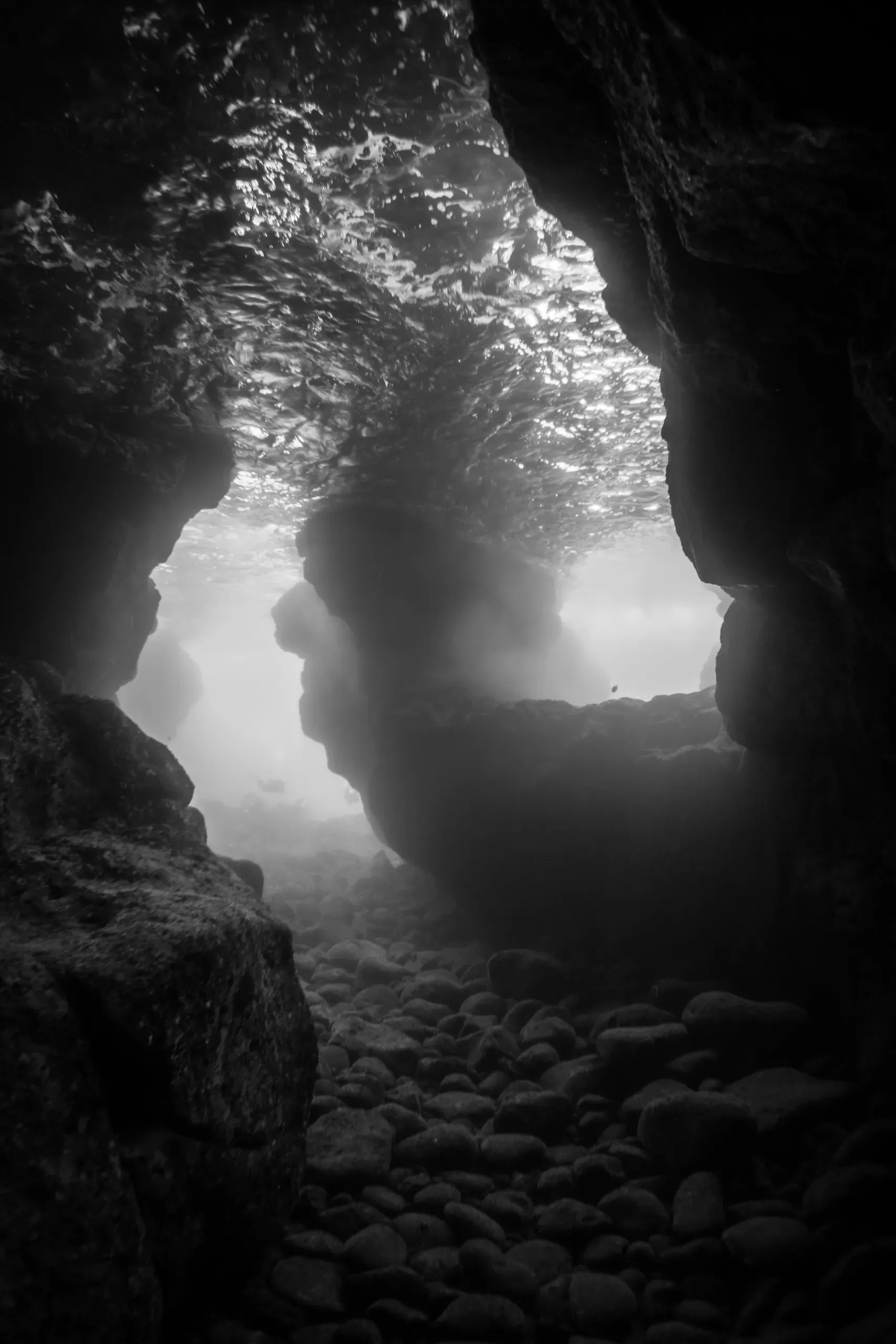 Black-and-white view from inside a cave toward a bright opening with rocky ground and water outside