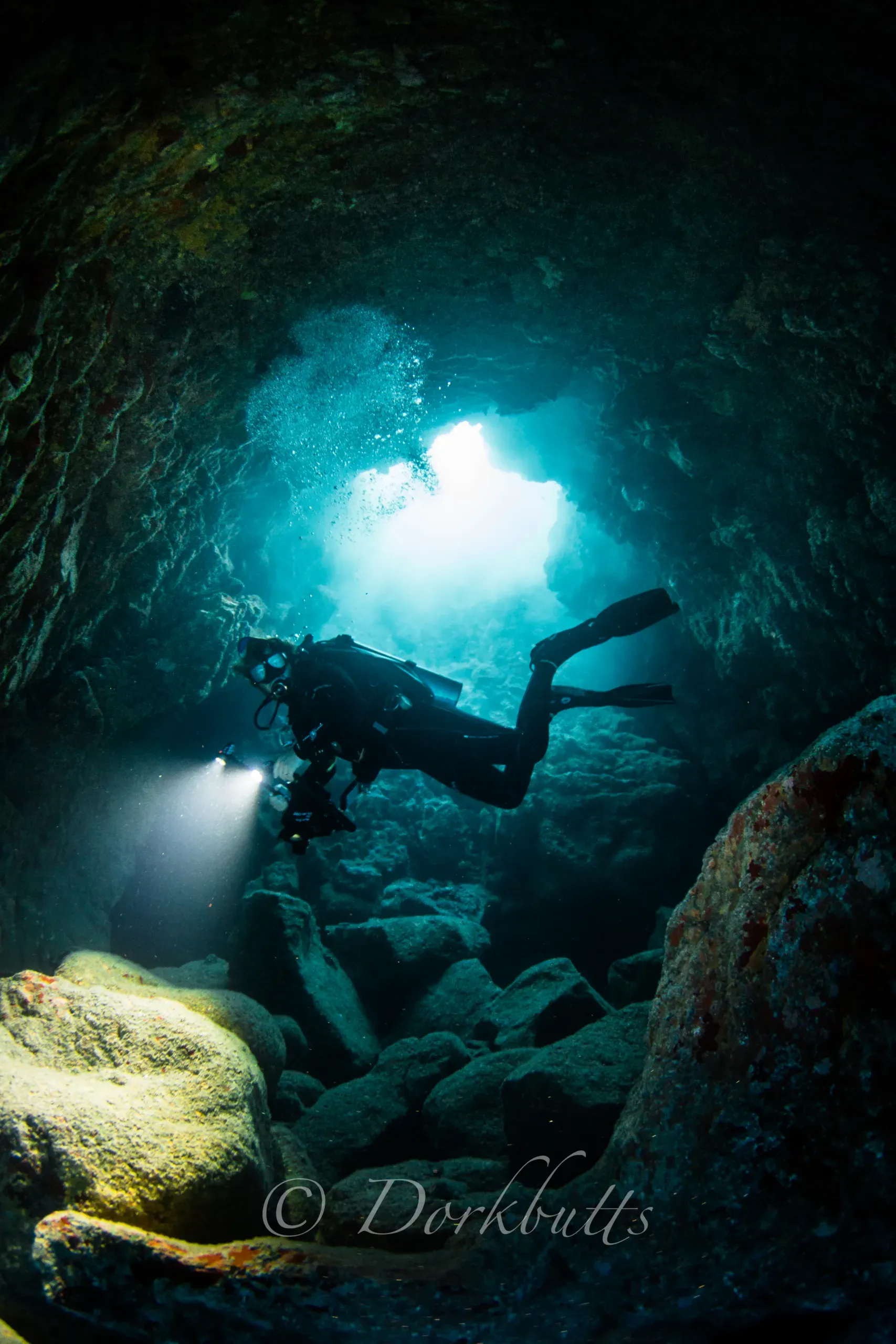 Scuba diver swimming through a dark underwater cave toward bright blue light above