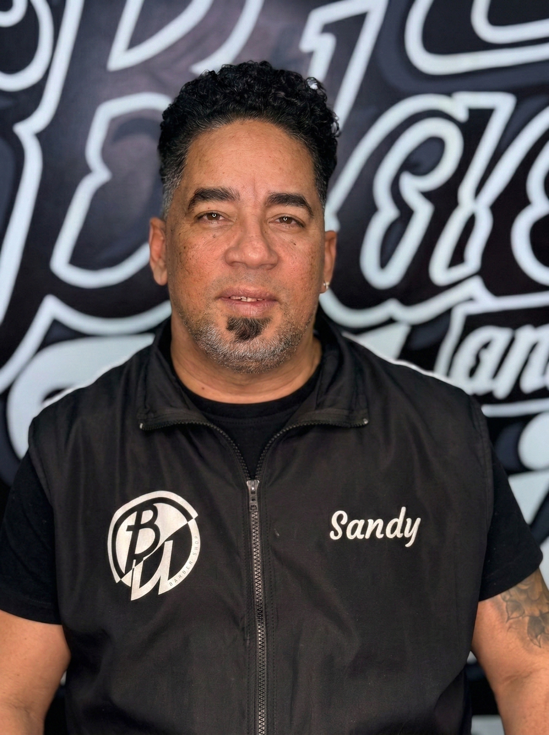 Man in black vest with “Sandy” on it, standing in front of a black and white logo.