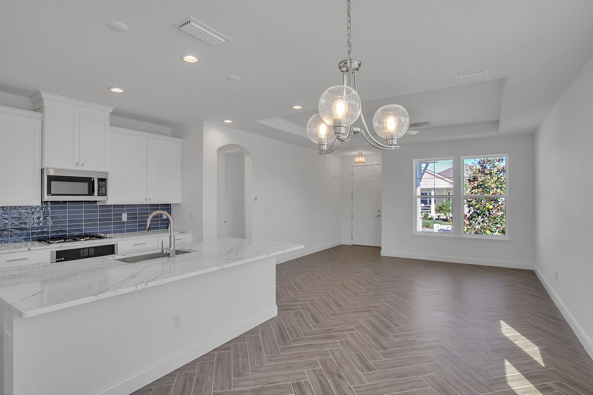 An empty living room with a kitchen and a chandelier.