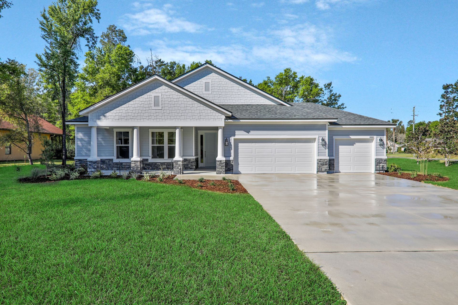 A large white house with two garage doors is sitting on top of a lush green lawn.