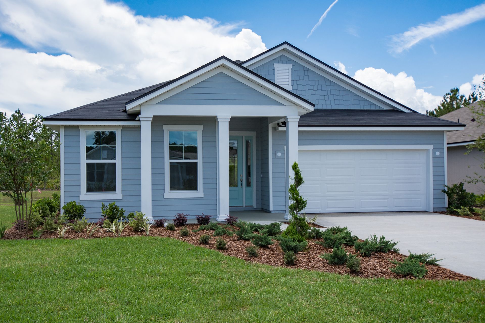 A blue house with a black roof and white trim is sitting on top of a lush green lawn.