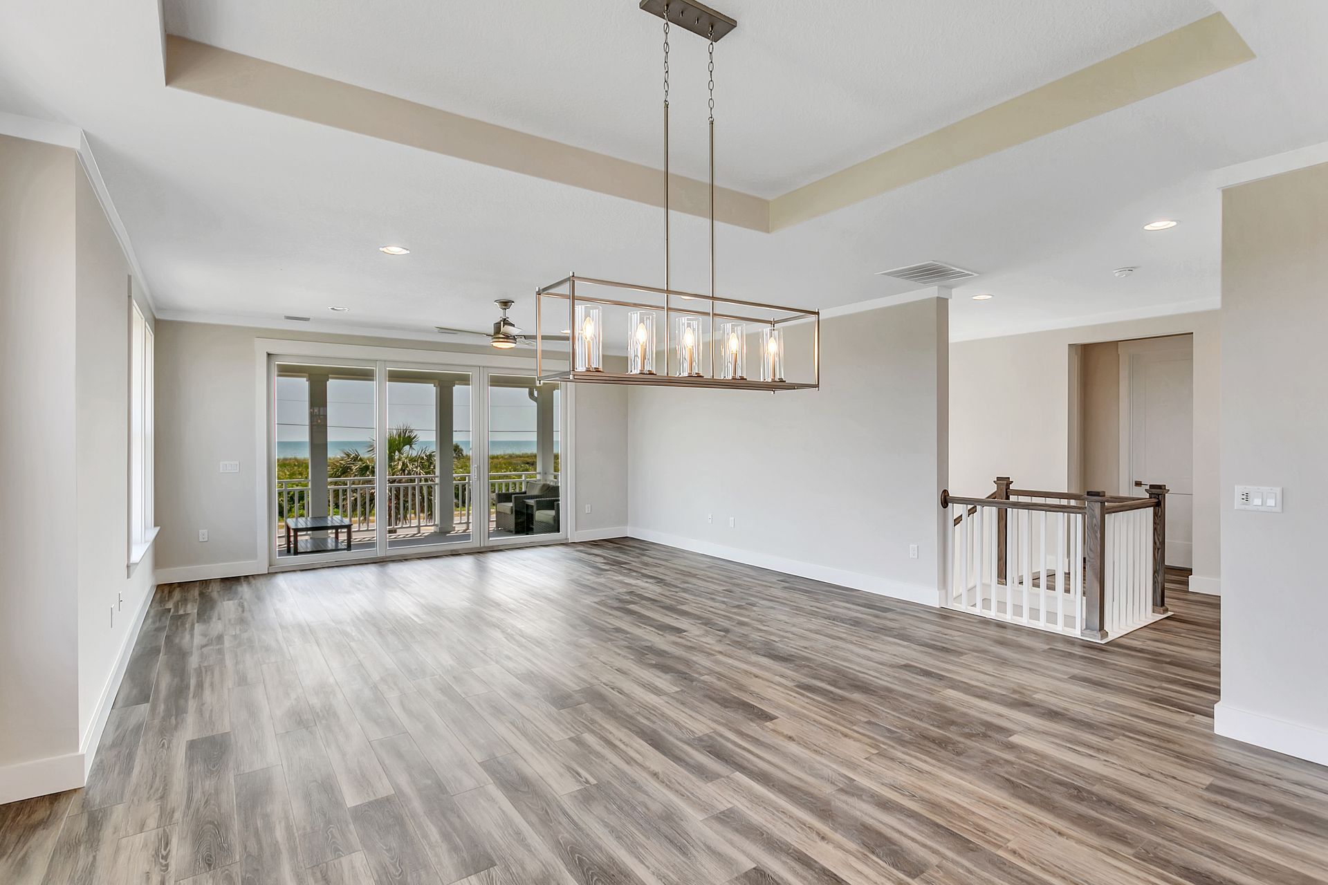An empty living room with hardwood floors and a chandelier hanging from the ceiling.