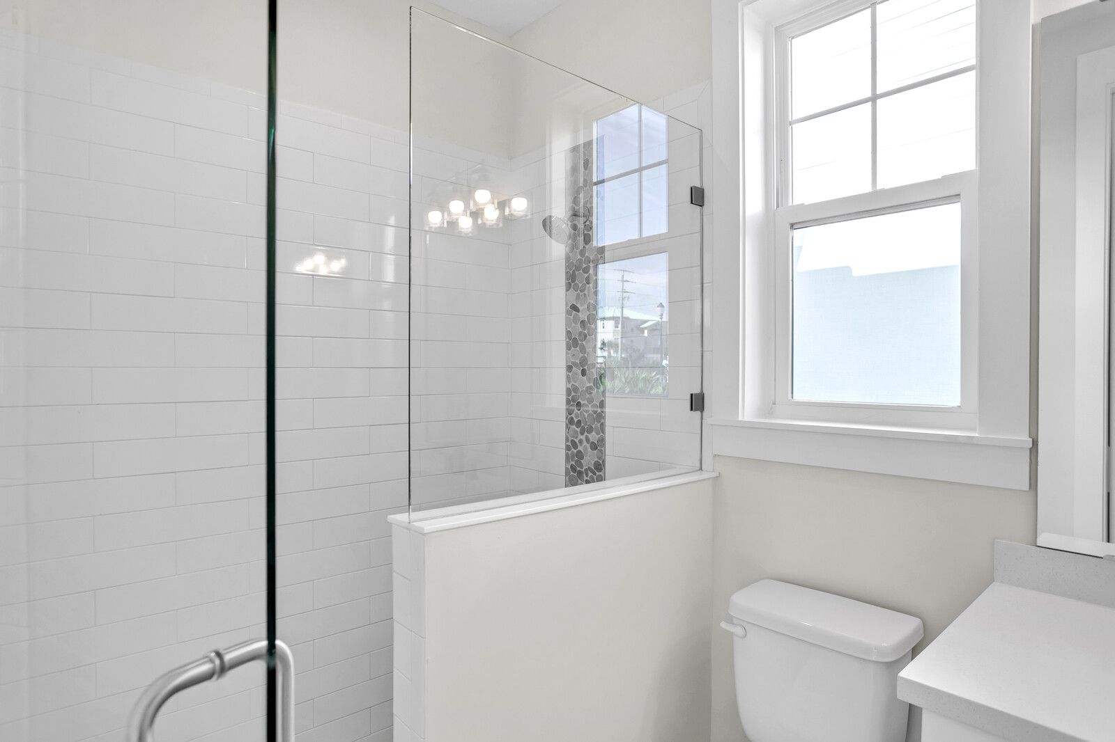 A bathroom with a toilet , shower , mirror and window.