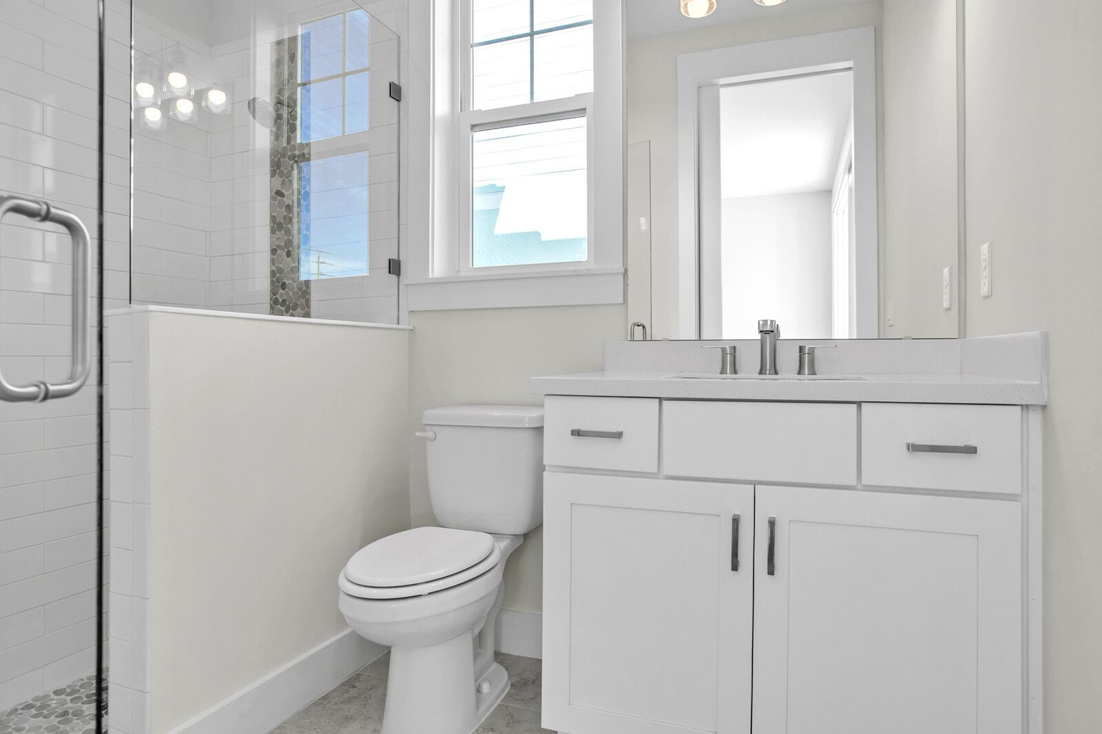 A bathroom with a toilet , sink , mirror and walk in shower.