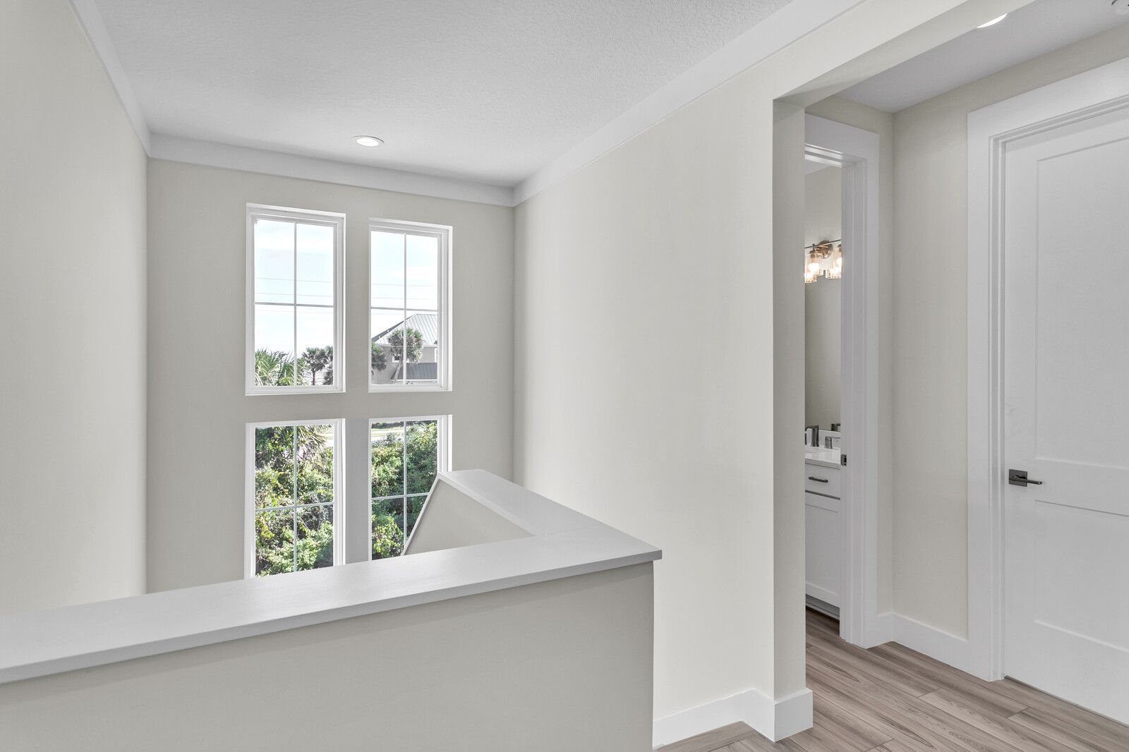 A hallway with a staircase leading to a bathroom and a window.