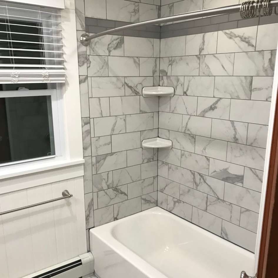 Bathroom with white marble-look tiles, a bathtub, shower rod, and built-in corner shelves. 
