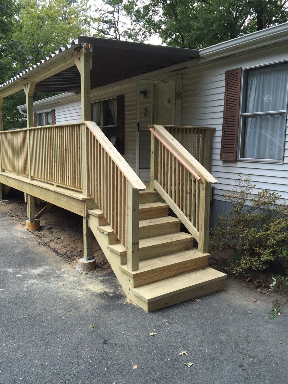 Wooden deck with steps leading up to a light-colored house with a dark awning.