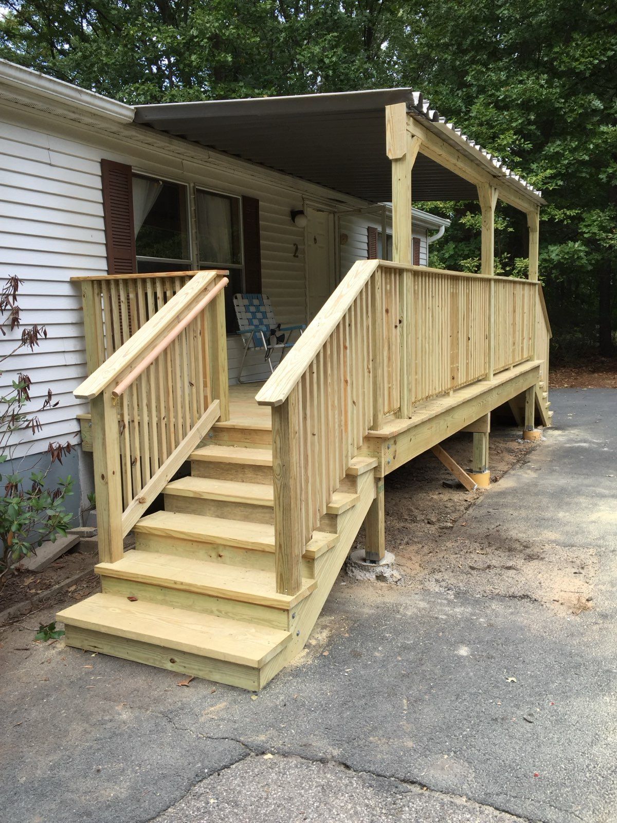 Wooden porch with steps and railing, attached to a white house with a brown awning.