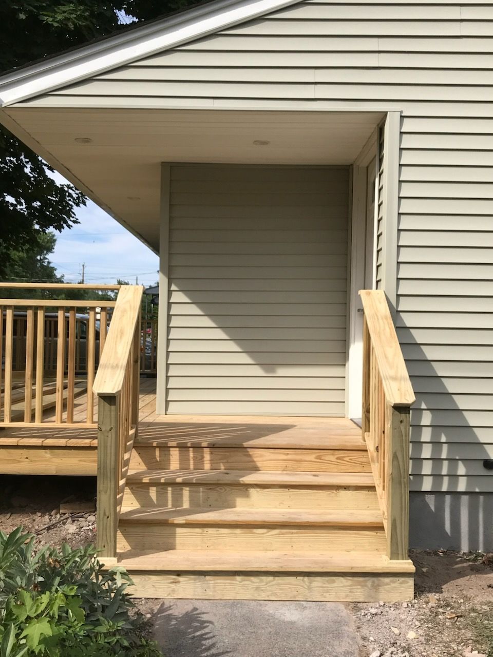 Wooden steps leading to a door under a light green awning on a house with light green siding.