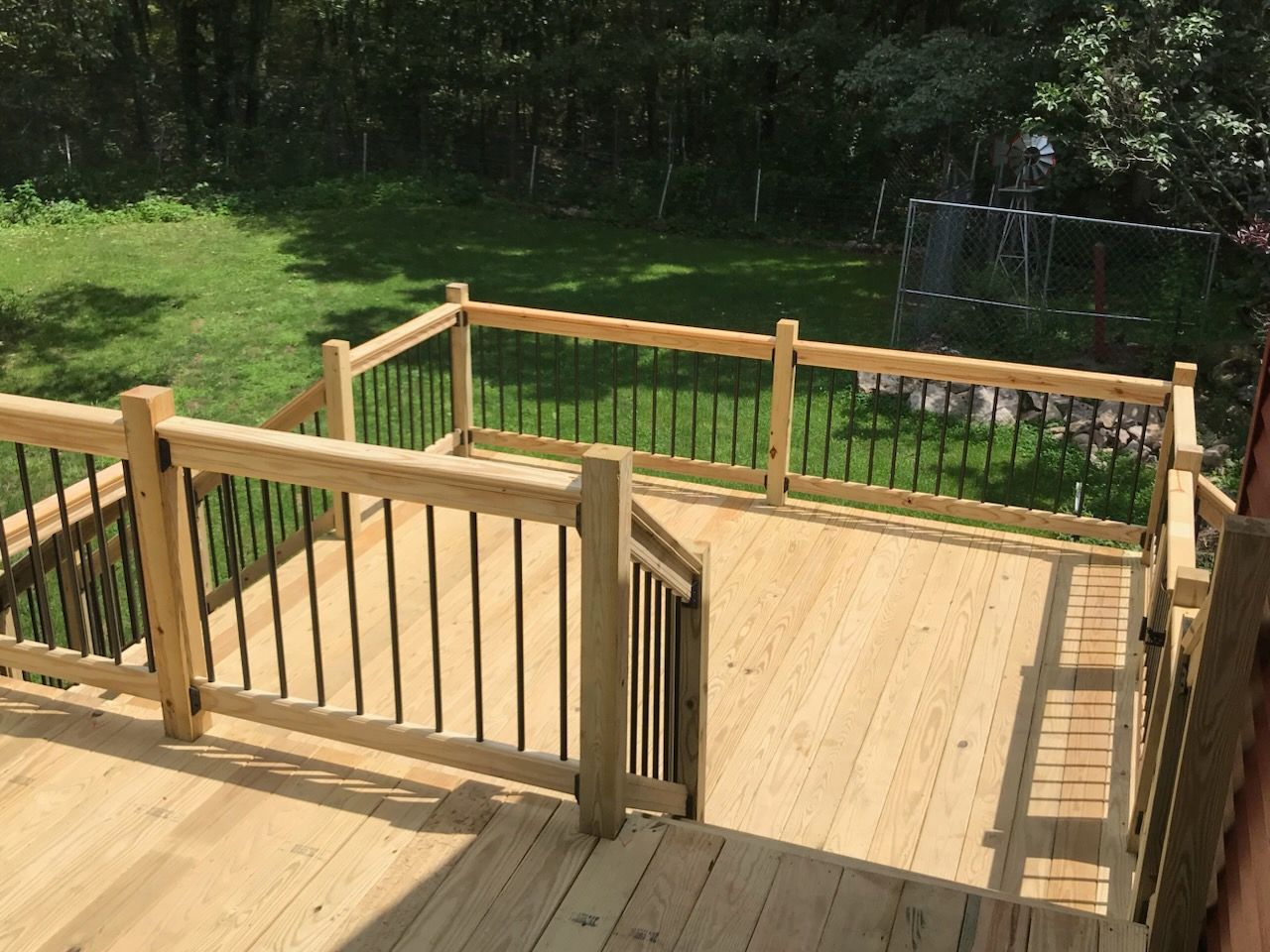Wooden deck with black railing and steps leading to grassy backyard.