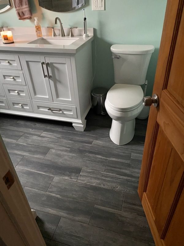 Bathroom with gray wood-look floor, white vanity and toilet, and teal wall. 