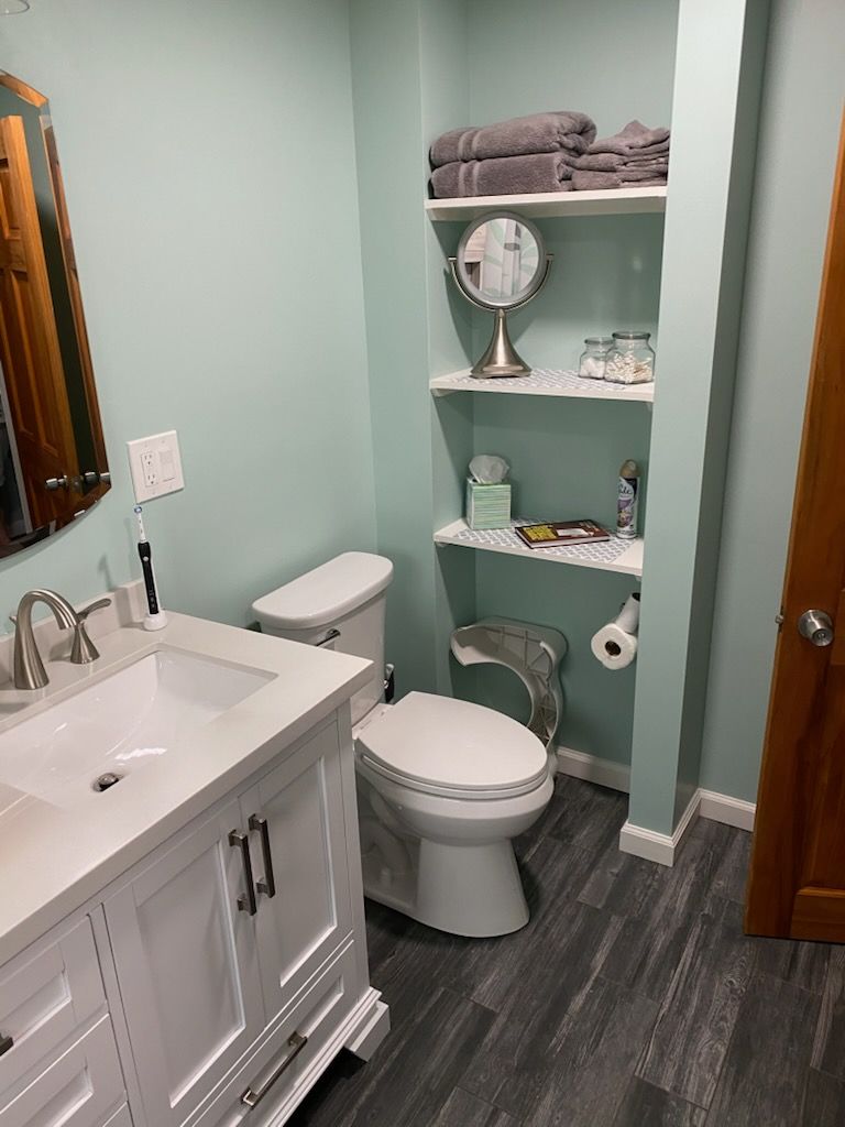 Bathroom with white vanity, toilet, and shelves with towels. 