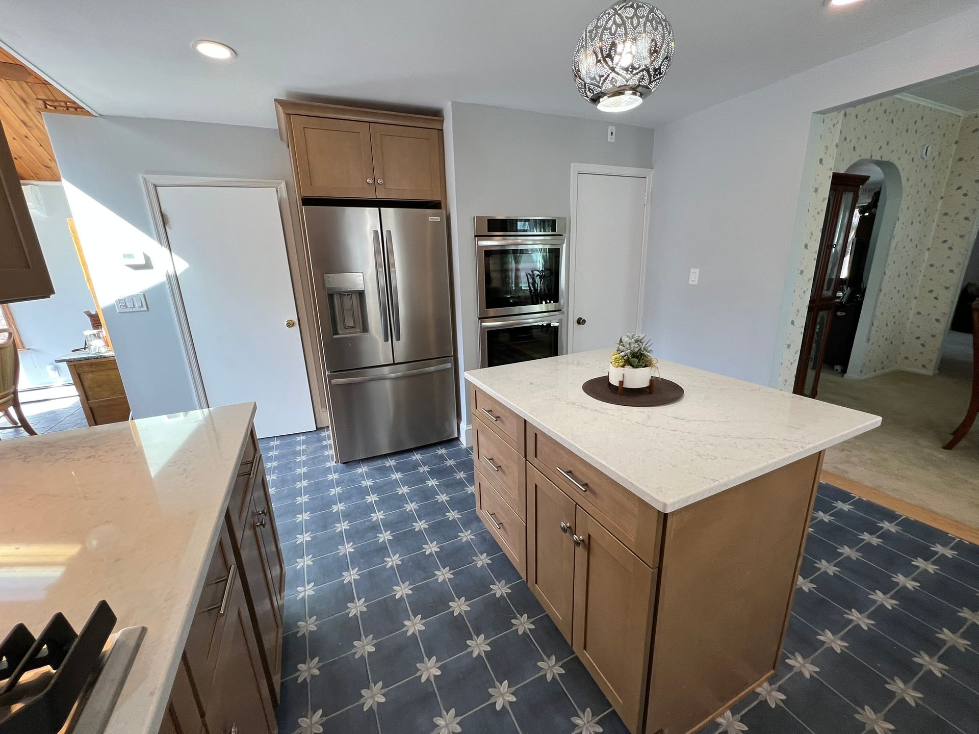 Kitchen with stainless steel appliances, brown cabinets, white countertops, and patterned blue floor tiles.