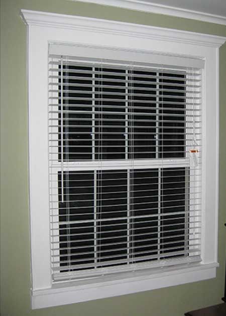 White-framed window with blinds, closed, set in a light green wall.