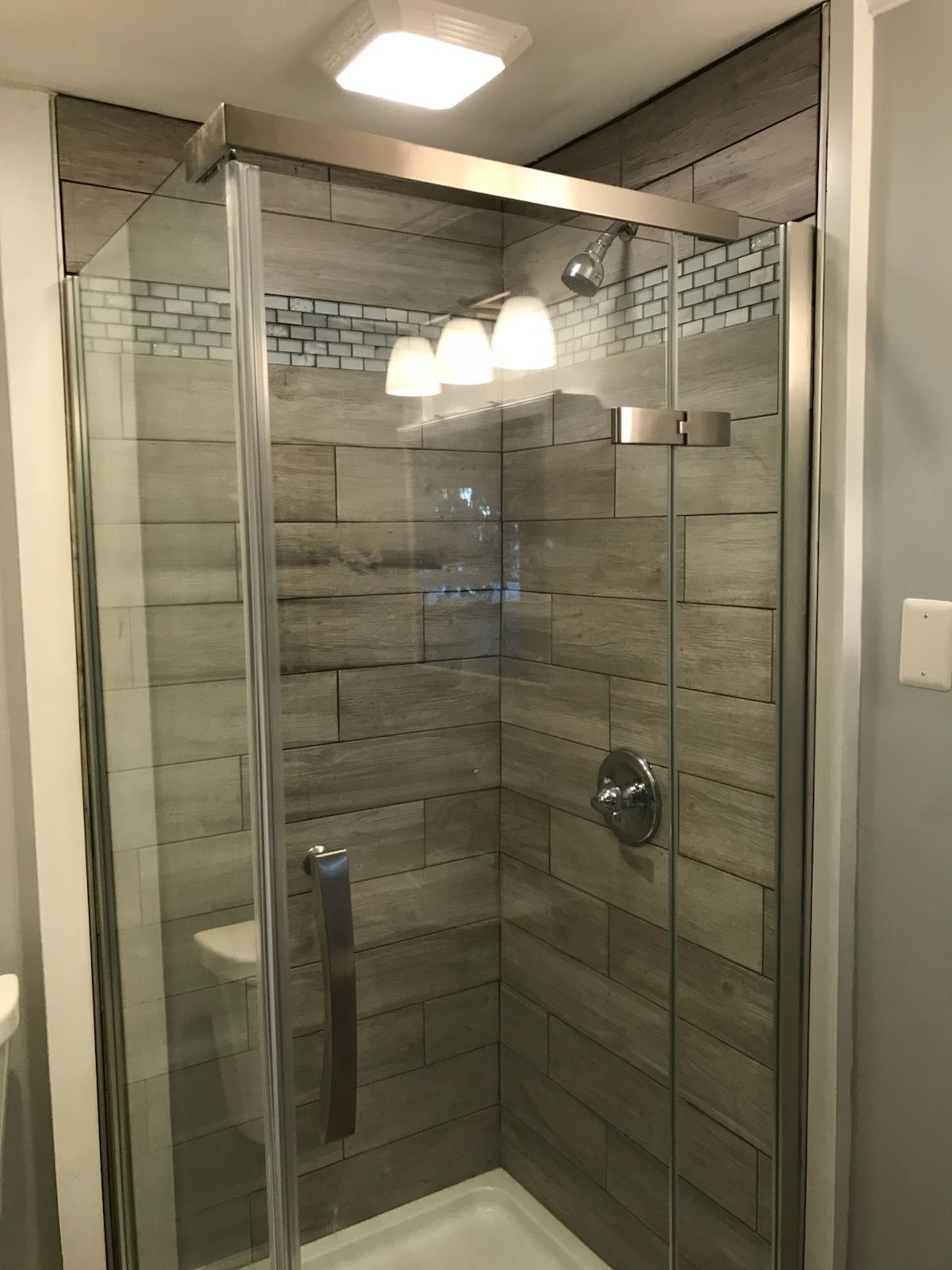 Shower with gray and blue tile, glass door, and silver fixtures.