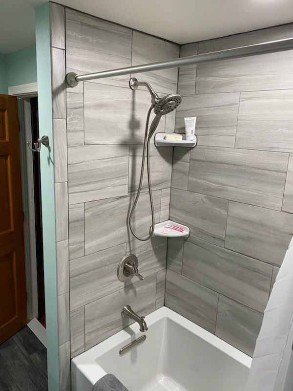 A shower with gray tiled walls, a white tub, and a silver showerhead and rod.