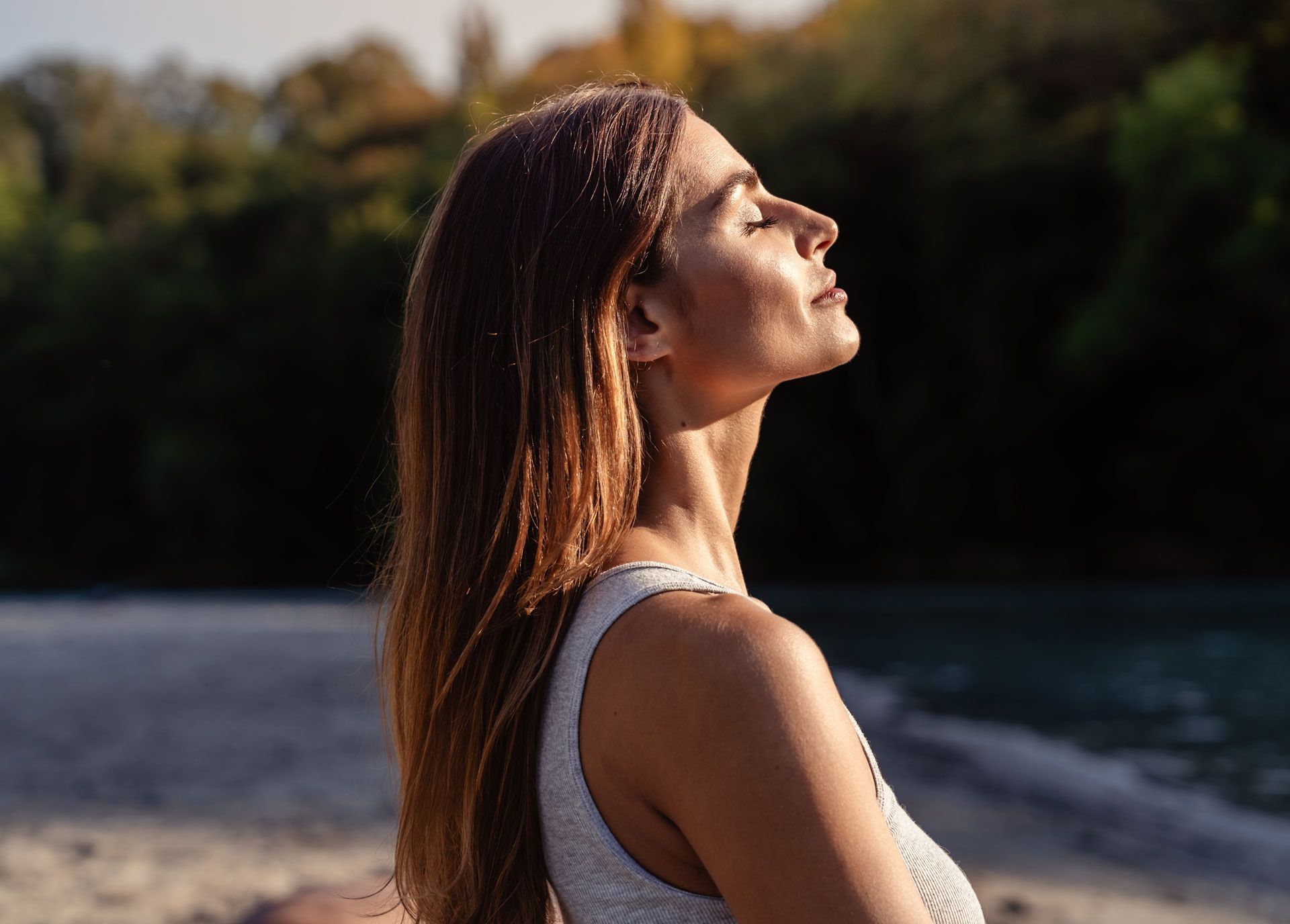 Woman with eyes closed, tilted head, sunlit, beach background.