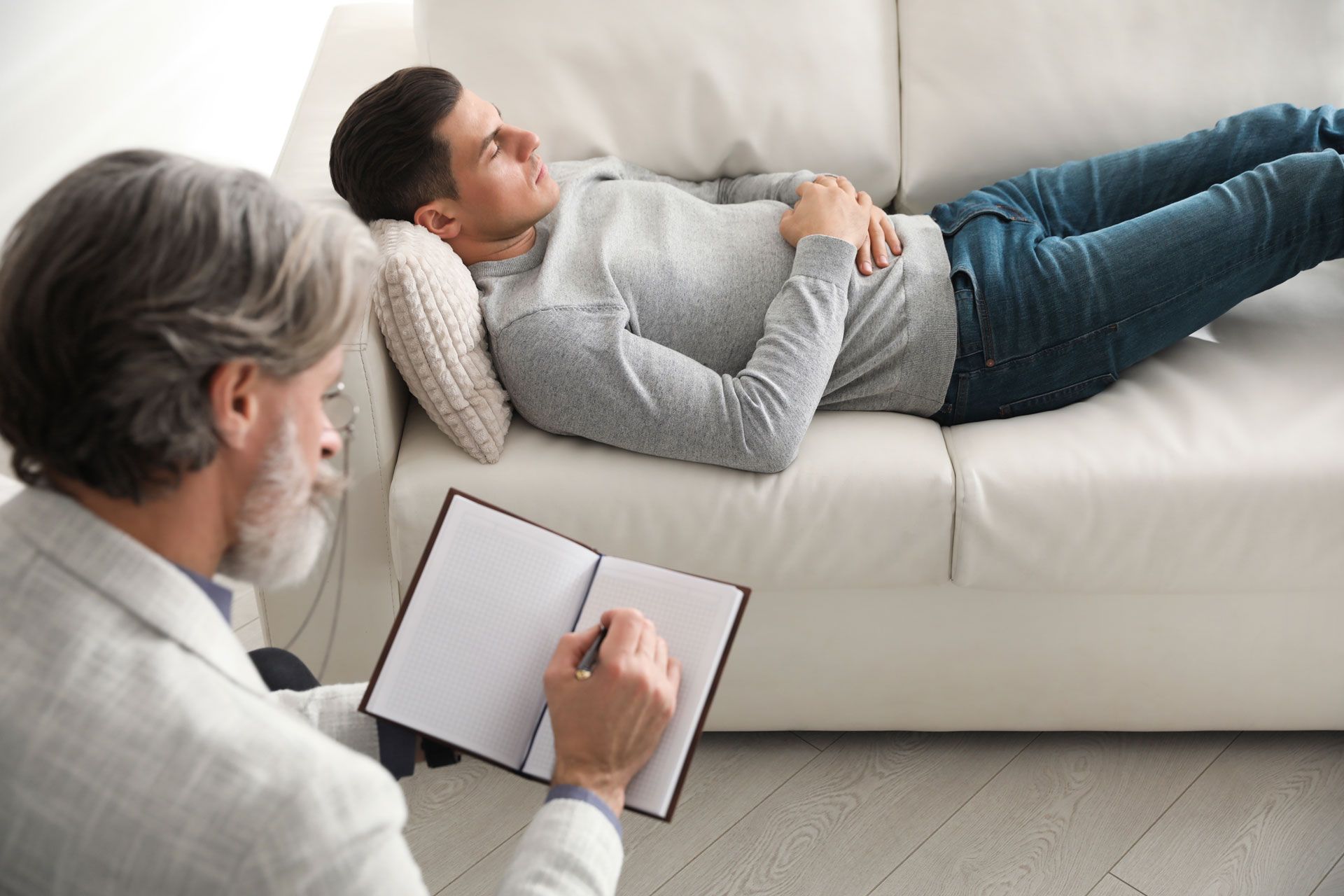Man reclining on a couch, speaking to a therapist who is taking notes.