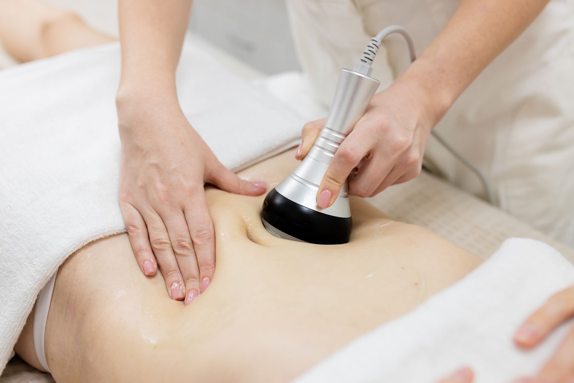 Person receiving abdominal skin treatment with a handheld device in a spa setting.