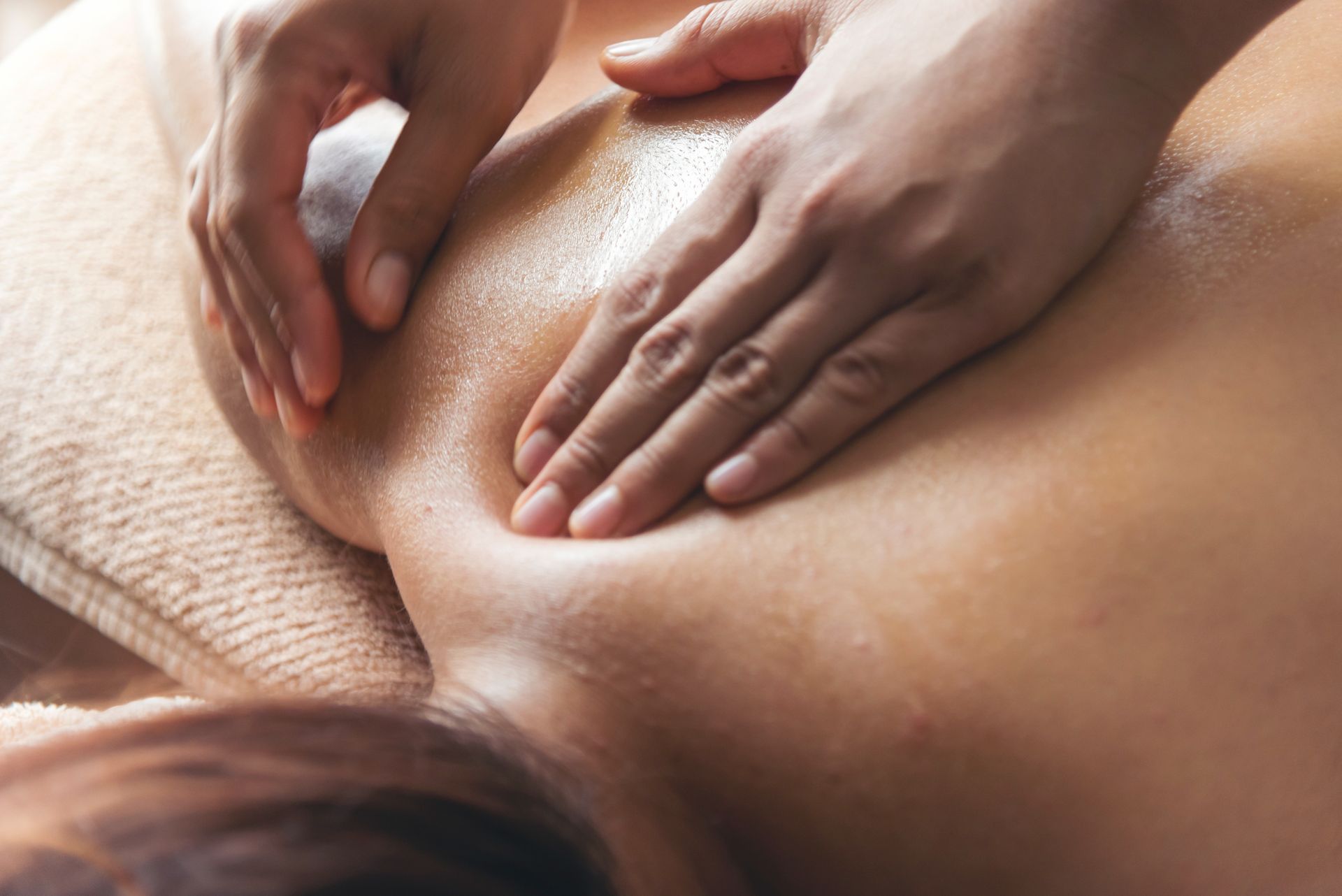 Hands massaging a back; close-up, oils visible, on a massage table.