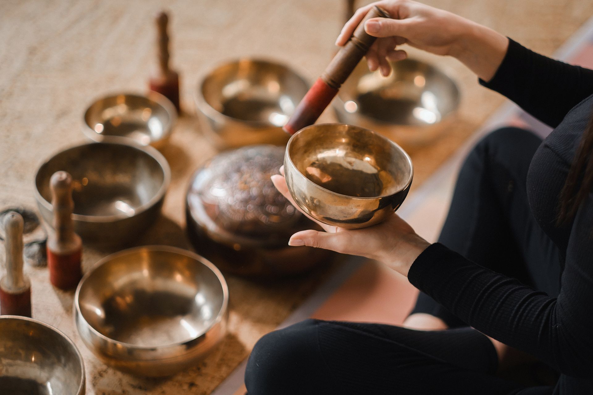 Person playing a Tibetan singing bowl with a mallet; several other bowls are nearby.