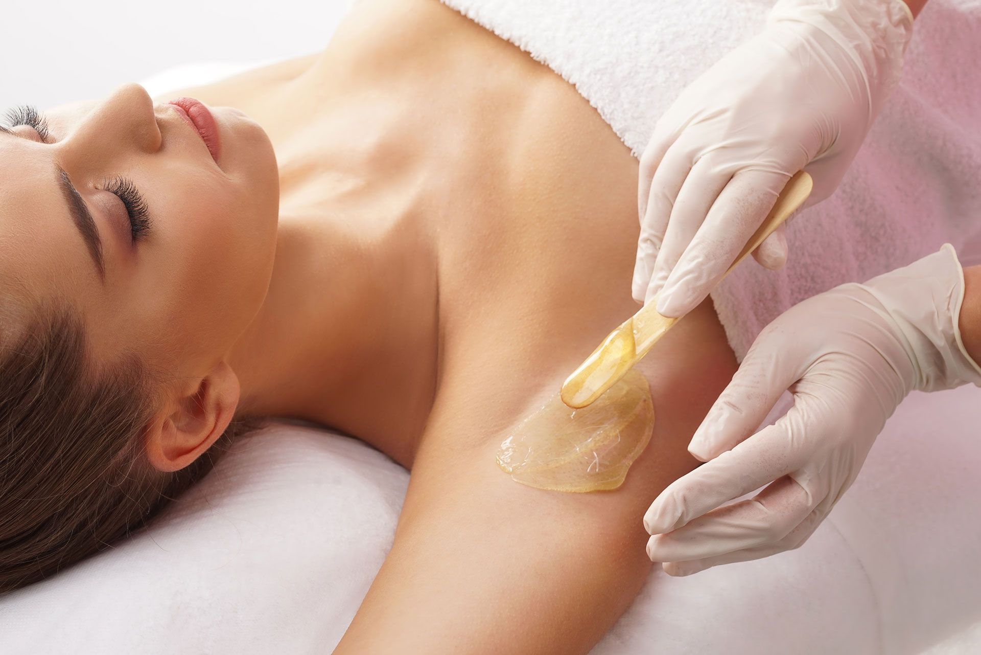 Armpit waxing with gloved hands applying wax.