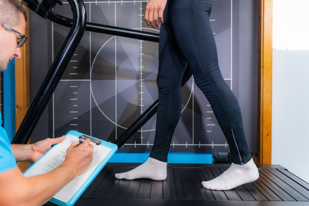 A Man Is Writing On A Clipboard While A Woman Is Walking On A Treadmill — Sandy Gugenberger Podiatrist in Port Macquarie, NSW
