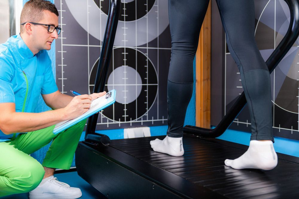 A Man Is Kneeling Down Next To A Woman On A Treadmill — Sandy Gugenberger Podiatrist in Port Macquarie, NSW