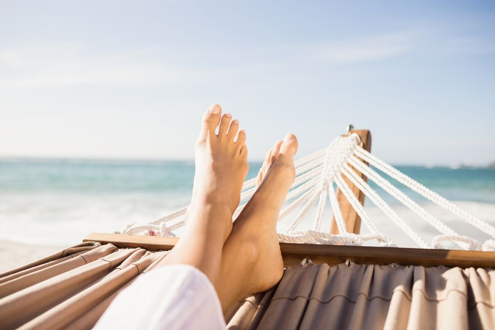 A Woman Is Laying In A Hammock On The Beach With Her Feet Up — Sandy Gugenberger Podiatrist in Port Macquarie, NSW