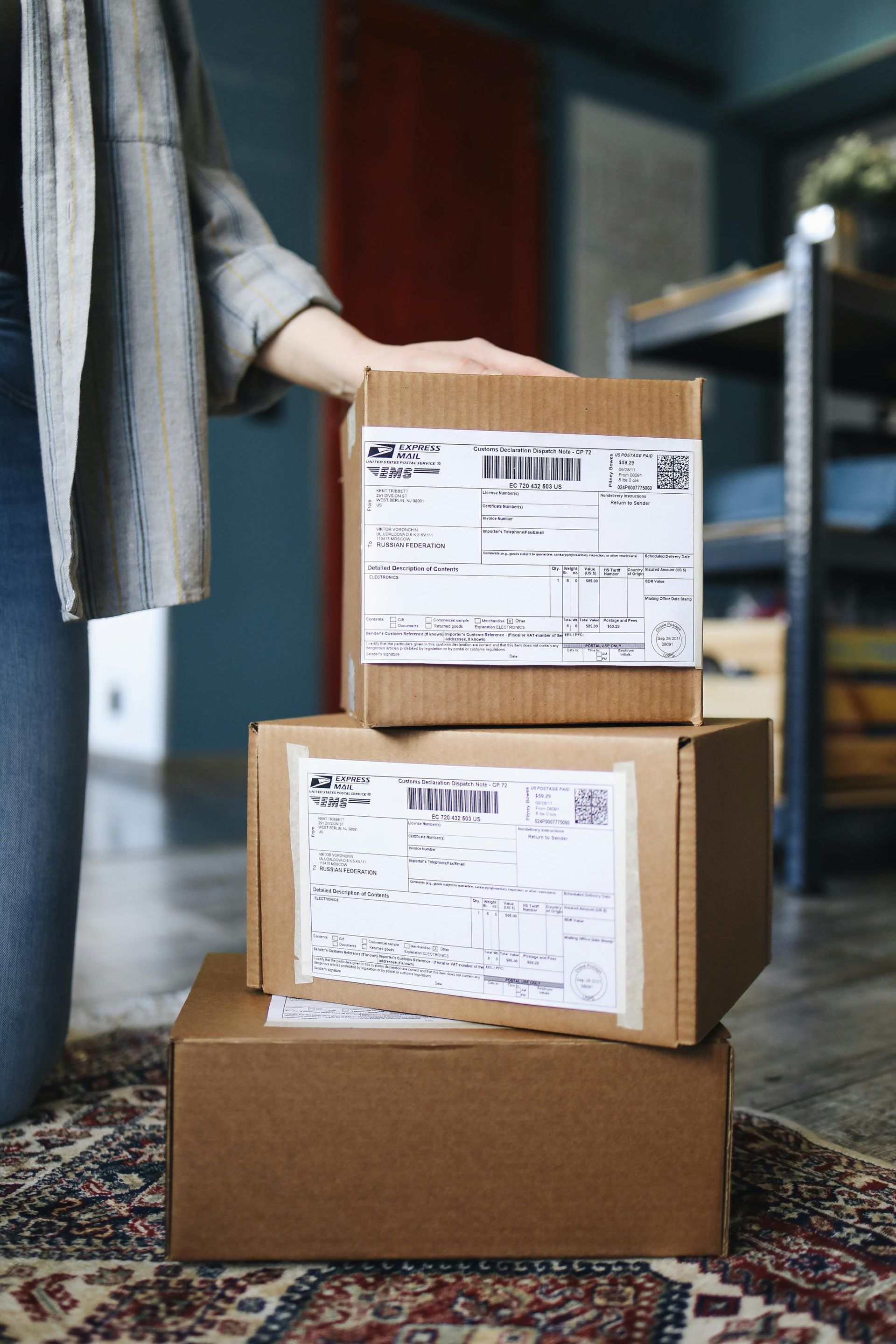 Person holding stack of return packages with shipping labels in warehouse setting.