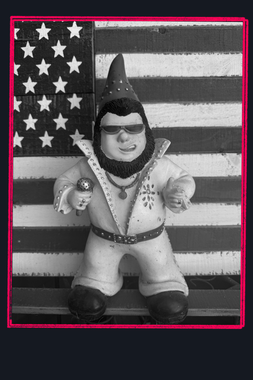 Elvis garden gnome in a studded jumpsuit, posed before an American flag backdrop.