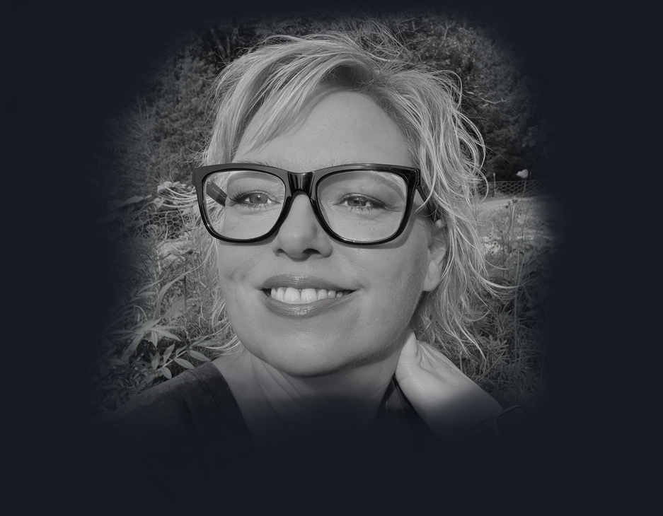 Black-and-white portrait of a smiling person with glasses against a dark background