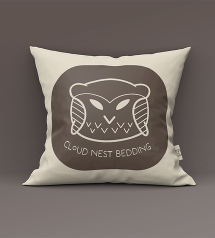 Cream pillow with a brown circular graphic of a sleeping bear and the text “CLOUD NEST BEDDING.”
