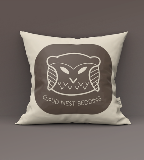 Cream pillow with a brown circular graphic of a sleeping bear and the text “CLOUD NEST BEDDING.”