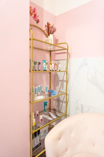 Una stanza rosa con uno scaffale dorato pieno di cosmetici e una sedia.
