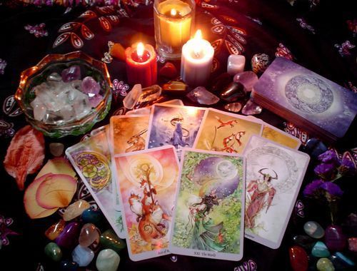 Tarot cards spread on a table with candles, crystals, and colorful stones.