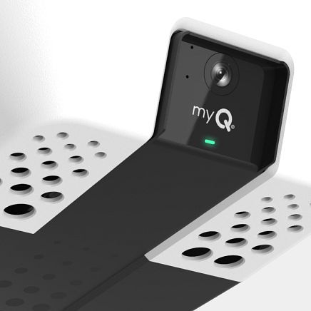 Black and white MyQ smart garage door camera with a green status light, mounted on a white surface.